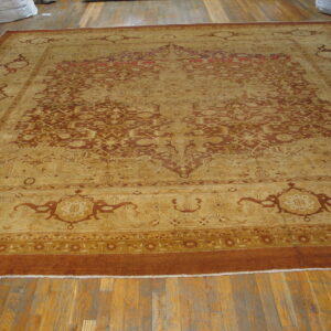 Large traditional gold and rust rug with an intricate medallion design displayed on worn hardwood floors.