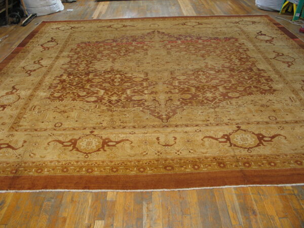 Large traditional gold and rust rug with an intricate medallion design displayed on worn hardwood floors.