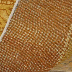 Close-up of a golden patterned rug, revealing its woven rust-colored backing on wood flooring.