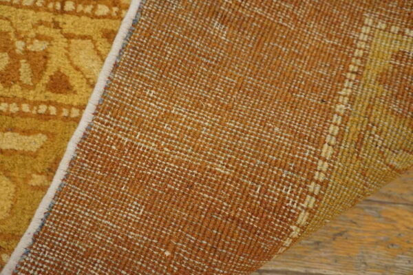 Close-up of a golden patterned rug, revealing its woven rust-colored backing on wood flooring.
