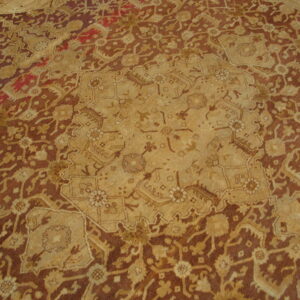 A textured rug featuring a complex traditional pattern in shades of brown, tan, gold, and hints of red.