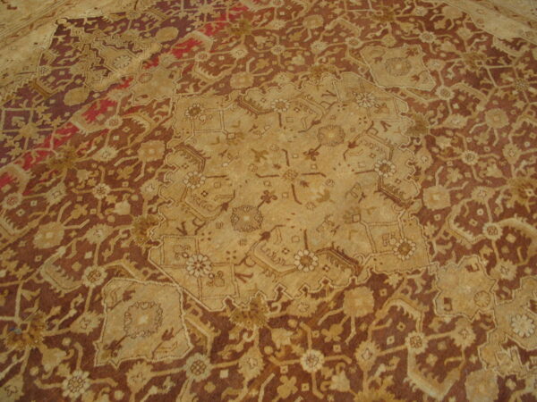 A textured rug featuring a complex traditional pattern in shades of brown, tan, gold, and hints of red.