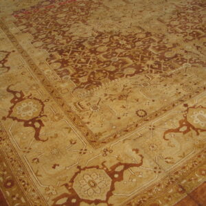 Angled view of a low-pile traditional rug with dense red-brown and tan geometric patterns and a detailed border.