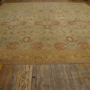 Oversized pale blue and gold traditional rug with rust accents rests on distressed wood flooring.