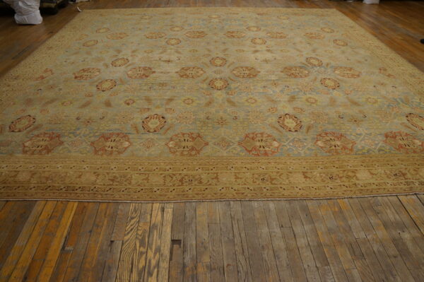 Oversized pale blue and gold traditional rug with rust accents rests on distressed wood flooring.