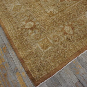Gold and beige traditional rug with intricate borders shown on distressed gray wood floor.