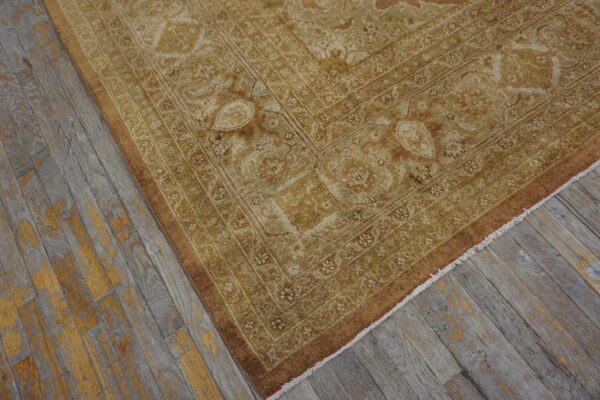 Gold and beige traditional rug with intricate borders shown on distressed gray wood floor.