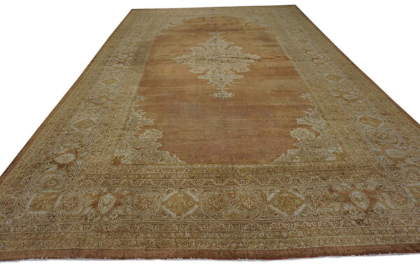 Large traditional rug featuring a copper field and elaborate tan and beige medallion and borders.