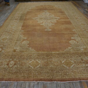 Distressed copper and cream traditional rug featuring an ornate medallion rests on gray wood flooring.