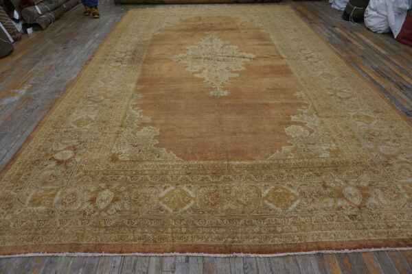 Distressed copper and cream traditional rug featuring an ornate medallion rests on gray wood flooring.