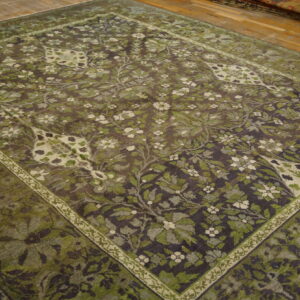 Dark, distressed floral area rug in shades of olive green and cream on light hardwood flooring.