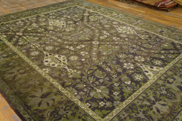Dark, distressed floral area rug in shades of olive green and cream on light hardwood flooring.