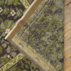 Dark green floral rug folded to show the backing and fringe resting on distressed wood flooring.