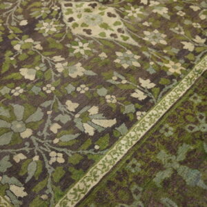 Dark rug featuring dense green and cream floral vines and a contrasting narrow patterned border.