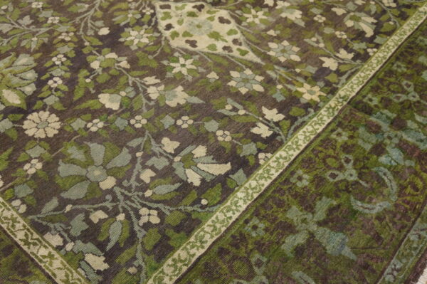 Dark rug featuring dense green and cream floral vines and a contrasting narrow patterned border.