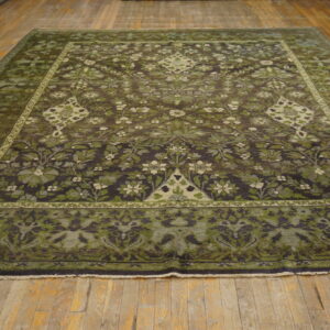 Square rug featuring dark olive and brown botanical motifs laid on distressed wooden floorboards.