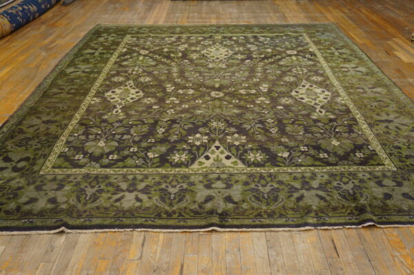 Square rug featuring dark olive and brown botanical motifs laid on distressed wooden floorboards.