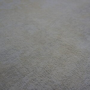 Solid neutral high-pile rug texture closeup, showing edges over dark brown wood floorboards.