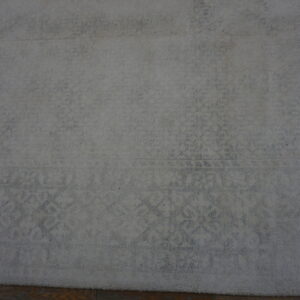 Textured, plush light gray rug with a subtle faded classical design, resting on wood planks.