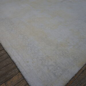 An off-white textured area rug with visible long pile covers dark, distressed wood flooring.
