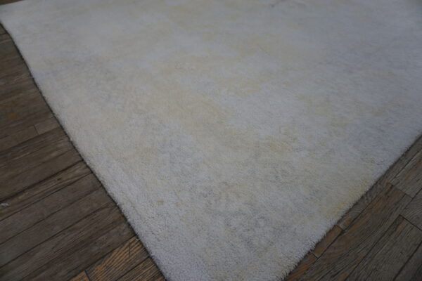 An off-white textured area rug with visible long pile covers dark, distressed wood flooring.