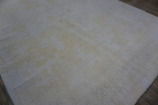 A light gray and cream distressed rug with subtle texture rests on dark brown wood plank flooring.
