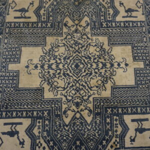 Low pile rug with a complex, dark blue and light tan geometric pattern and stylized birds.