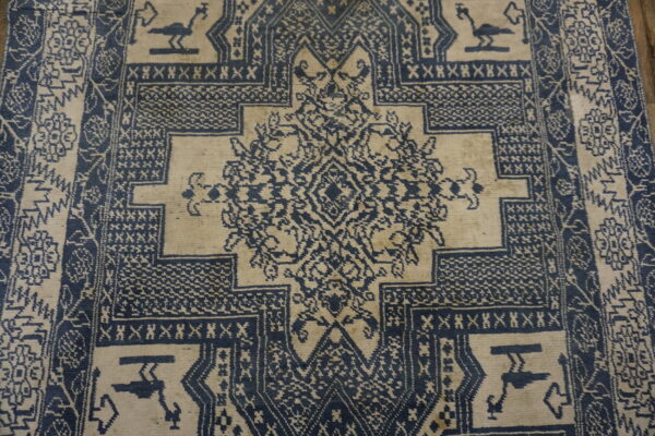 Low pile rug with a complex, dark blue and light tan geometric pattern and stylized birds.