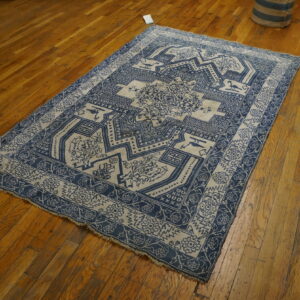 A rectangular low-pile rug with a detailed blue and beige geometric pattern rests on polished hardwood floors.