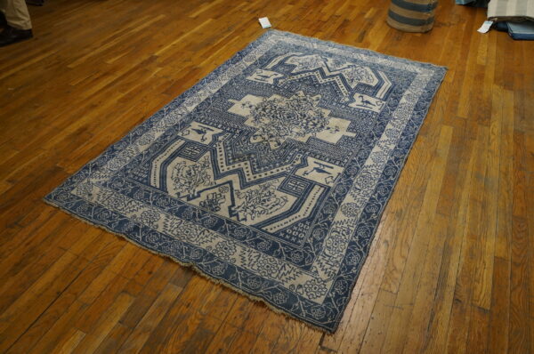 A rectangular low-pile rug with a detailed blue and beige geometric pattern rests on polished hardwood floors.