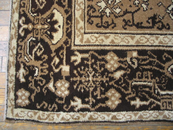 Ornate floral rug border in dark brown, tan, and cream lies partially on a wood plank floor.