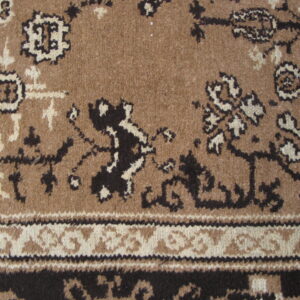 Traditional rug pattern in brown, black, and cream, featuring a dense pile texture and detailed border.
