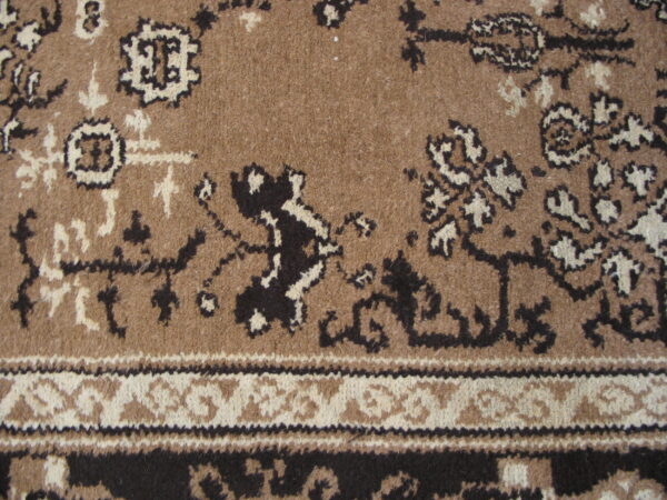 Traditional rug pattern in brown, black, and cream, featuring a dense pile texture and detailed border.