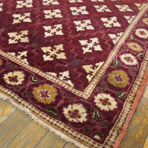 Deep red rug featuring cream geometric motifs and a wide floral border on light wood planks.