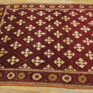 A deep red rug featuring beige geometric motifs and floral borders lies on a light wooden floor.