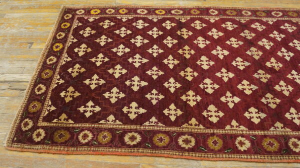 A deep red rug featuring beige geometric motifs and floral borders lies on a light wooden floor.