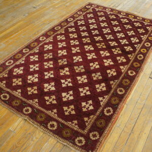 Low-pile maroon rug with a repeating beige geometric design rests on wide plank wood flooring.