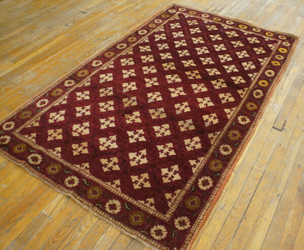 Low-pile maroon rug with a repeating beige geometric design rests on wide plank wood flooring.