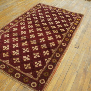 Burgundy rug with cream lattice and floral borders rests on rustic, wide plank wood flooring.