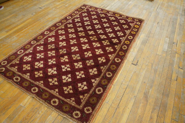Burgundy rug with cream lattice and floral borders rests on rustic, wide plank wood flooring.