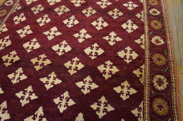 A high-pile burgundy rug featuring cream diamond motifs and a floral border on wood flooring.