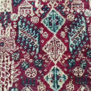 Burgundy rug detail showing geometric diamond motifs and ornate patterns in cream and teal blue.