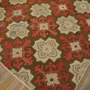 Diagonal view of a textured rug with red, beige, and olive floral medallions on distressed wood floor.