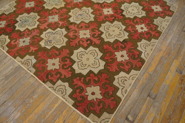 Repeating red, brown, and cream geometric pattern rug resting on distressed hardwood plank flooring.