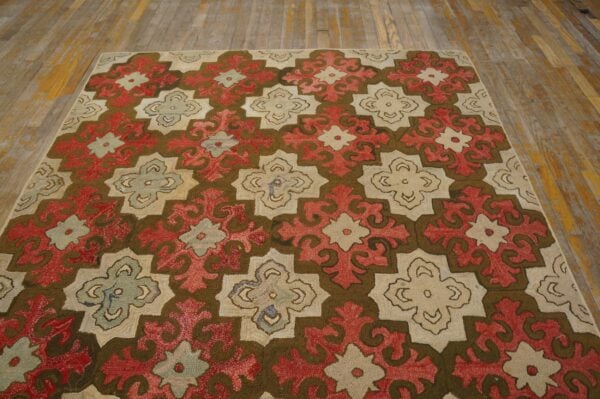 Repeating red, cream, and dark brown geometric pattern rug sits on rustic wooden flooring.