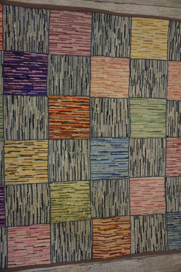 Textured, checkerboard rug using colorful horizontal squares and alternating vertical blocks of gray and black loops on a wood floor.