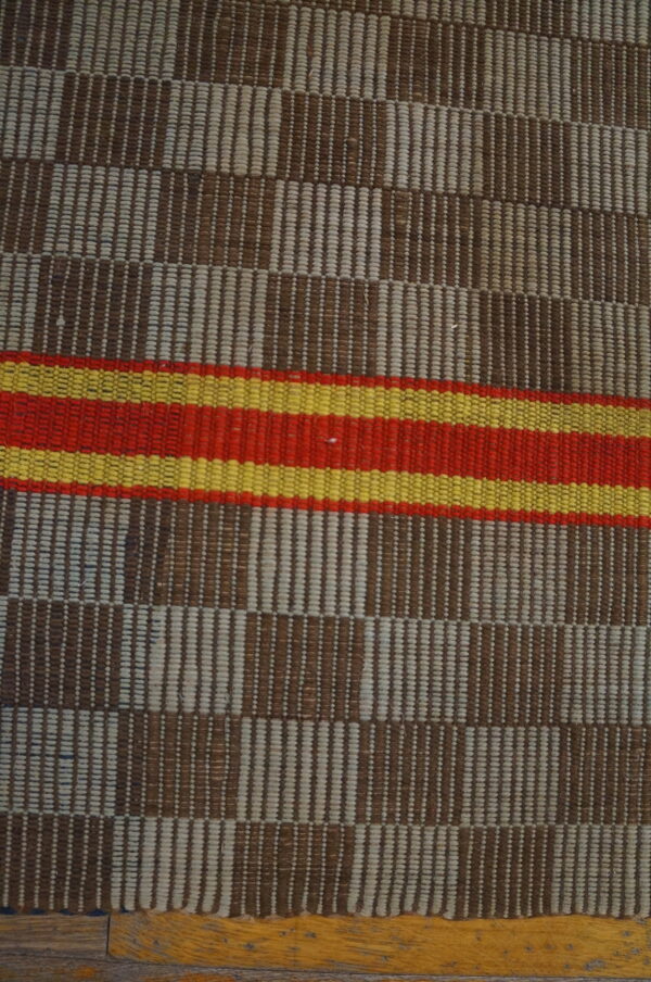 Woven rug with brown and beige vertical striped blocks, accented by horizontal red and yellow bands.