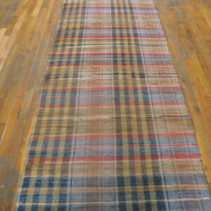 Muted red, blue, tan, and yellow plaid flatwoven runner rug lying on light hardwood flooring.