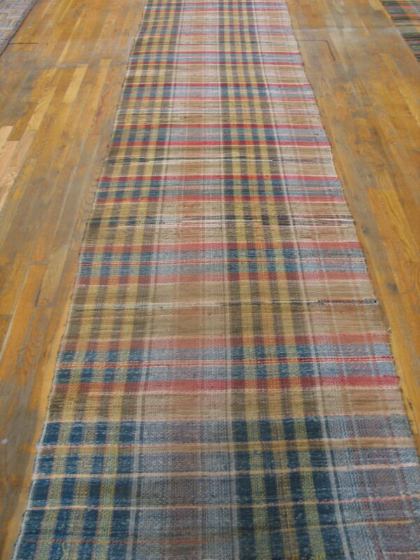 Muted red, blue, tan, and yellow plaid flatwoven runner rug lying on light hardwood flooring.