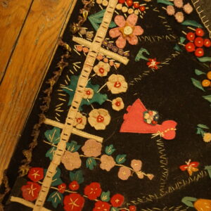 Black textile featuring colorful red, pink, and green floral and figurative appliqué on wide wooden planks.